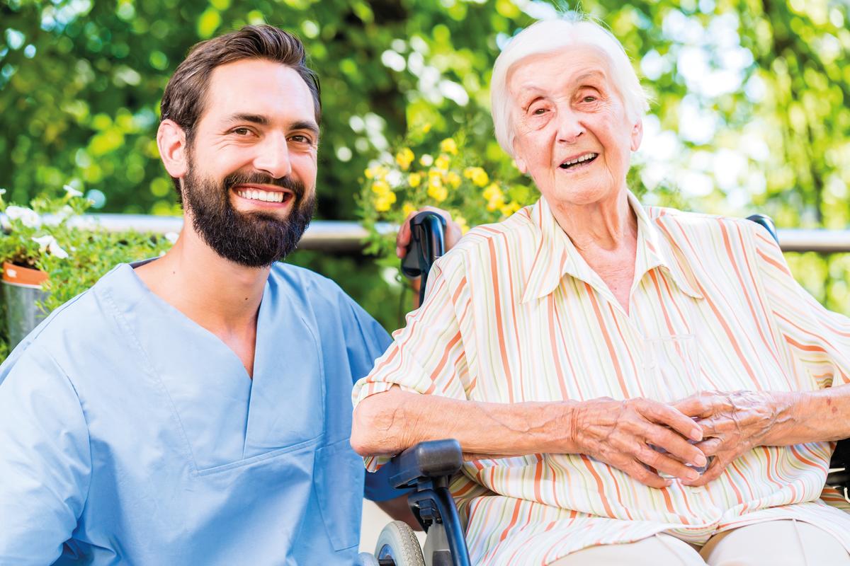 Ein Altenpfleger und eine ältere Dame lächeln zufrieden in die Kamera