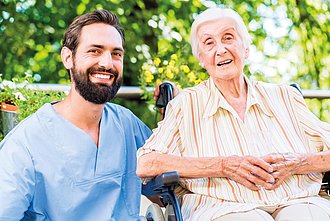 Ein Pfleger und eine älter Frau lächeln in die Kamera