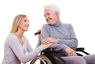 Eine Frau lächelt eine andere Frau an die im Rollstuhl sitzt